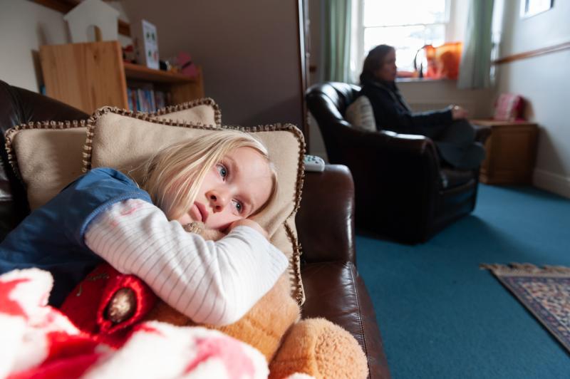 Image of a little girl lying on a sofa with an adult in the background.